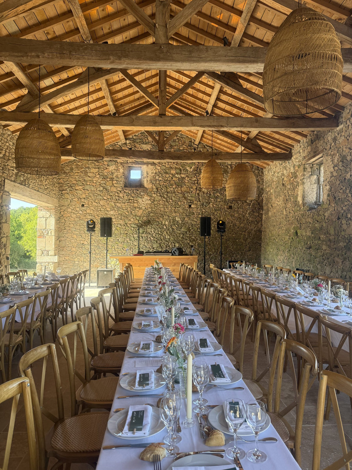 Salle en pierre aux poutres apparentes, tables dressées et sonorisation installée